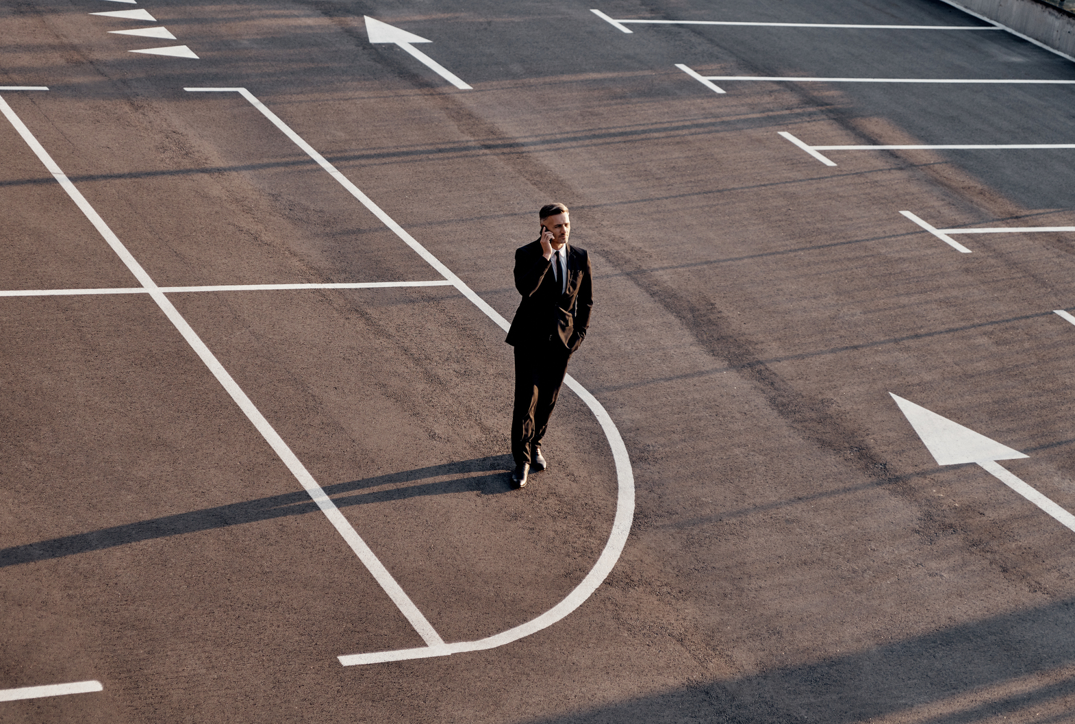 Top view of man in formalwear talking on mobile phone while standing on parking lot with arrow sign on it